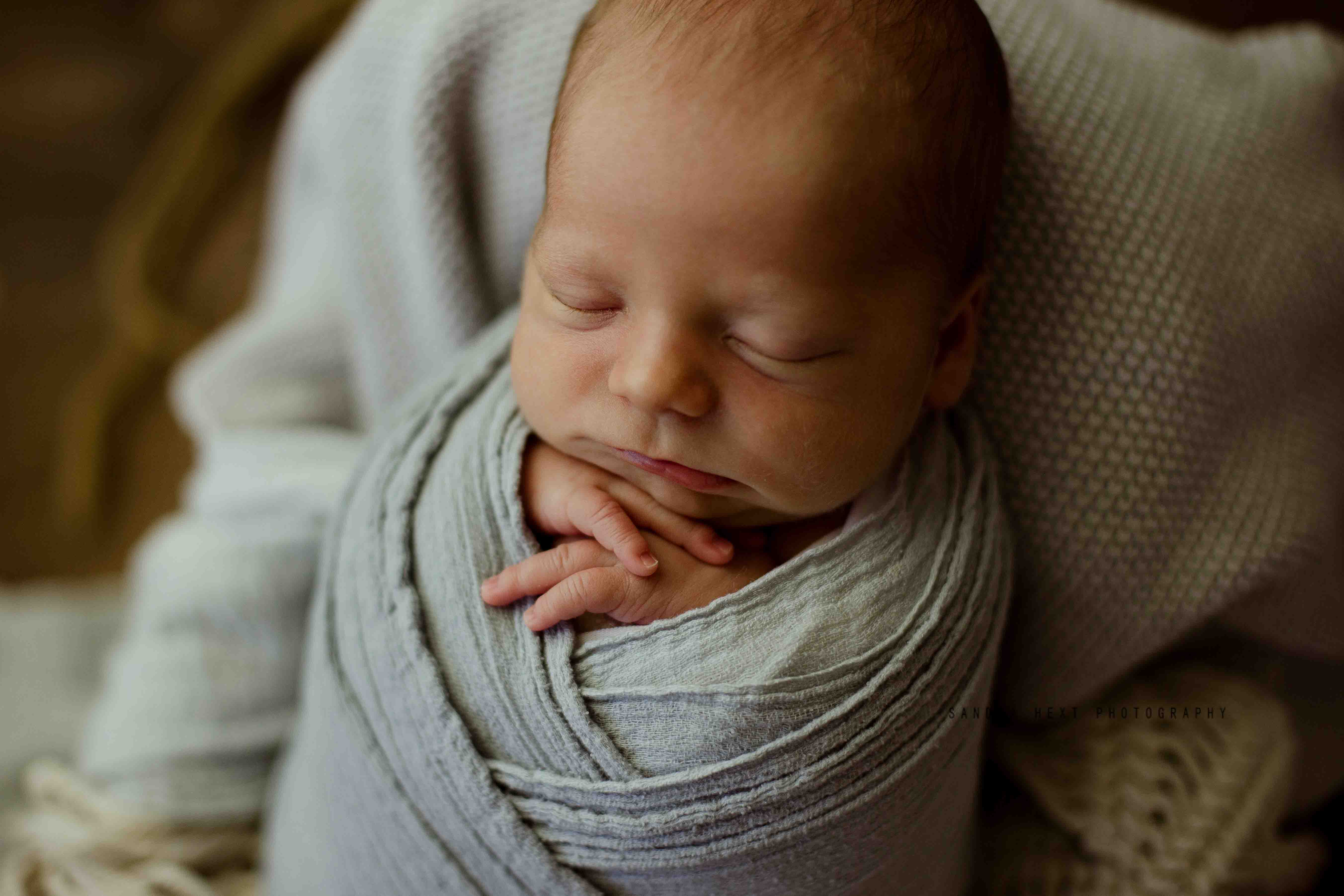 Sandra Hext Photography – Newborn baby girl photography – snuggled in soft neutral beige tones, holding a tiny bear, wrapped in a delicate mauve wrap. A warm and timeless portrait capturing pure sweetness.